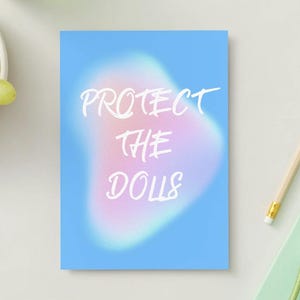 Może przedstawiać: Prostokątny wydruk z jasnoniebieskim tłem oraz miękką, rozmytą różowo-białą aurą pośrodku. Biały napis "PROTECT THE DOLLS" został nadrukowany stylizowaną, odręczną czcionką na środku tej rozmytej, kolorowej plamy.
