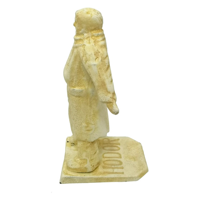 May include: A white cast iron doorstop shaped like a person with the word "Hodor" written on the base.