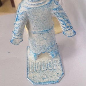 May include: A blue and white figurine of a person wearing a robe. The figurine is standing on a base with the word "Honor" written on it.