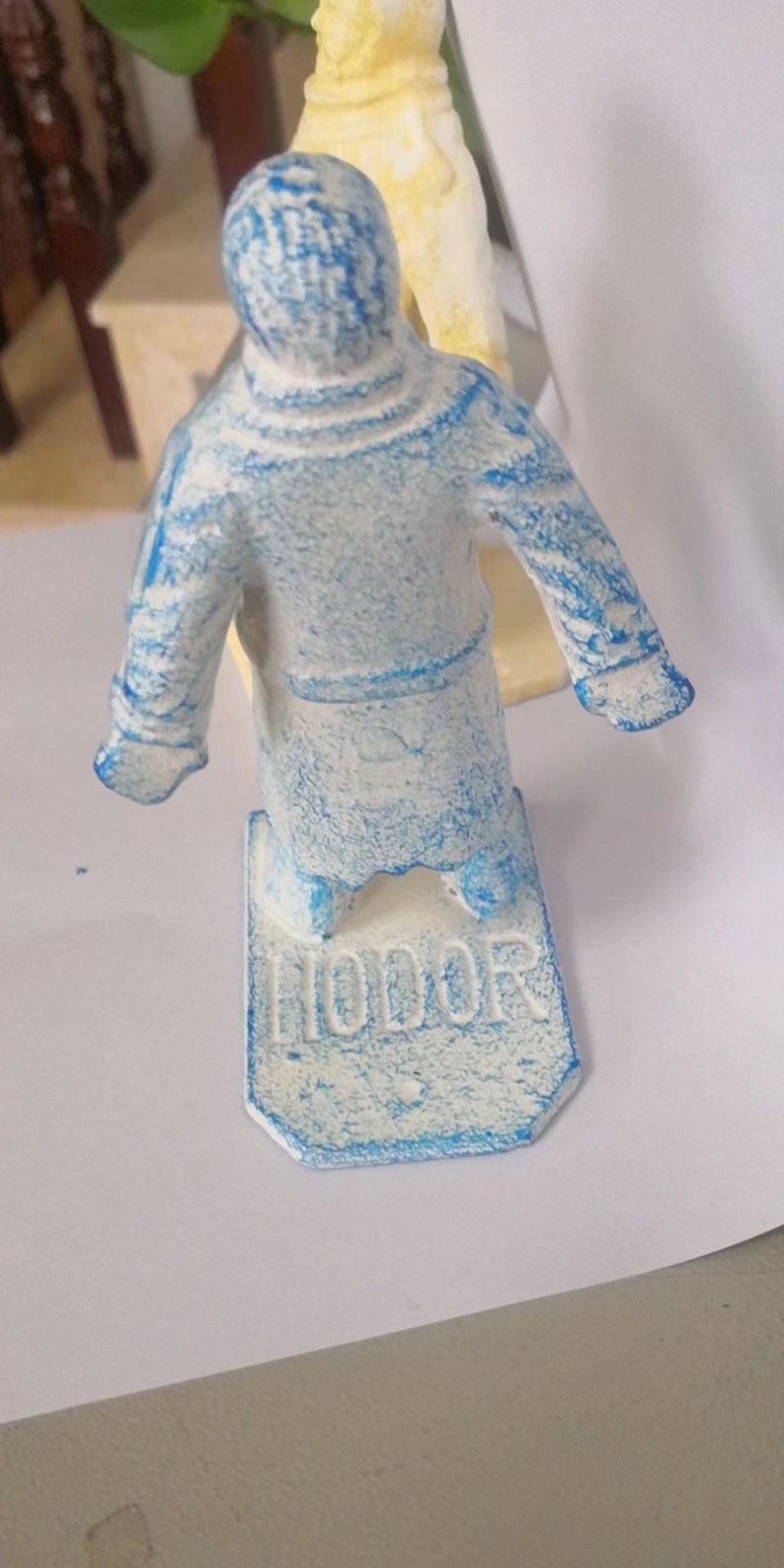 May include: A blue and white figurine of a person wearing a robe. The figurine is standing on a base with the word "Honor" written on it.