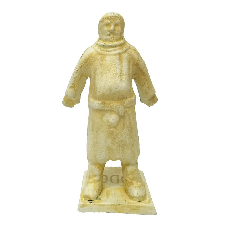 May include: A white cast iron figurine of a person wearing a long robe and a hood. The figurine is standing on a square base with the word "DODO" inscribed on it.