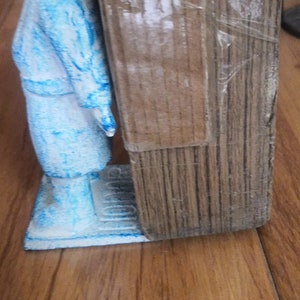 May include: A blue ceramic figurine of a person standing on a base. The figurine is next to a wooden doorstop.