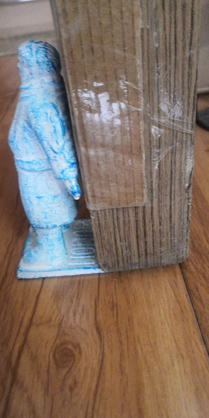 May include: A blue ceramic figurine of a person standing on a base. The figurine is next to a wooden doorstop.