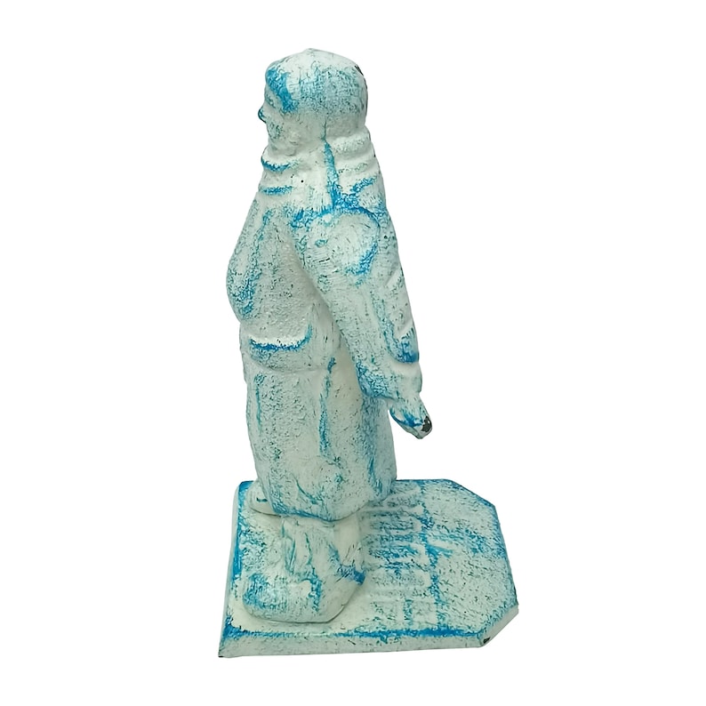 May include: A white cast iron figurine of a person wearing a blue and white winter coat standing on a base. The figurine is painted in a distressed white finish with blue accents.