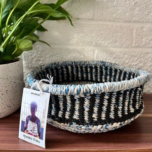 May include: A woven basket with black, white and blue stripes. The basket is made by Apeeba Baba.