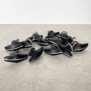 May include: A collection of black cabinet knobs with a silver trim and a metal screw. The knobs have a unique, curved design. The knobs are scattered on a light-colored surface.