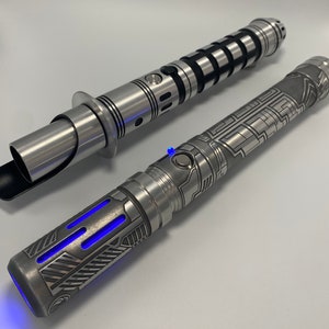 May include: Two silver lightsabers with intricate designs. One lightsaber has a black handle and a silver blade. The other lightsaber has a silver handle with a blue light at the end.