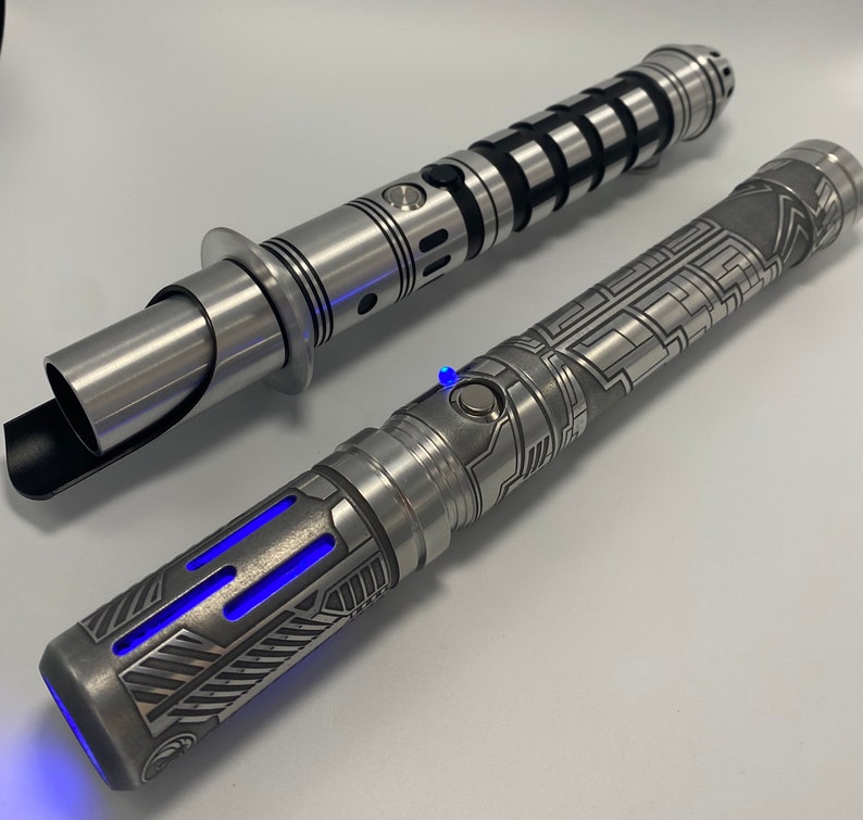 May include: Two silver lightsabers with intricate designs. One lightsaber has a black handle and a silver blade. The other lightsaber has a silver handle with a blue light at the end.