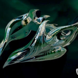 May include: A silver-colored, abstract, organic-shaped sculpture with a sharp, pointed design. The sculpture is made of a smooth, reflective material and has a dark green background.