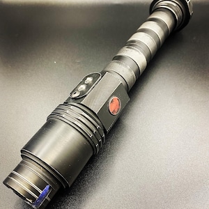May include: A black lightsaber prop with a red button and a textured grip. The lightsaber is made of metal and has a black and silver finish.