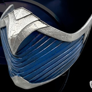 May include: A blue and silver mask with a layered, textured design. The mask has a curved shape with a silver trim and a series of parallel lines on the blue surface. The top portion features a layered silver design.