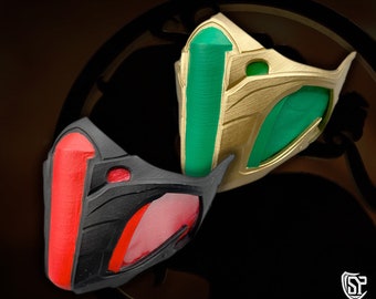 Peut inclure: Deux masques, l'un noir avec des accents rouges et l'autre doré avec des accents verts. Les deux masques sont stylisés et ont un design futuriste.