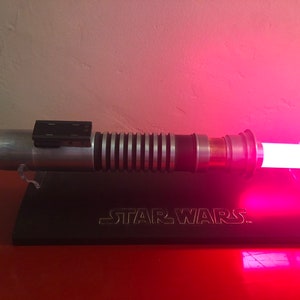May include: A silver lightsaber with a pink blade, on a black stand with the words "STAR WARS" engraved on it.