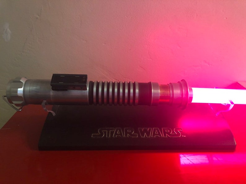 May include: A silver lightsaber with a pink blade, on a black stand with the words "STAR WARS" engraved on it.