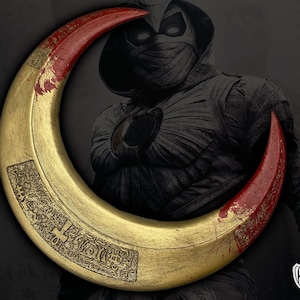 May include: A gold crescent-shaped weapon with red tips, possibly a prop from a movie or comic book. The weapon has engraved details and is set against a dark background with a character in the background.