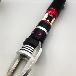 May include: A black and silver tool with a red accent and a claw-like end. The tool has a silver ring around the middle and a red button on the side.