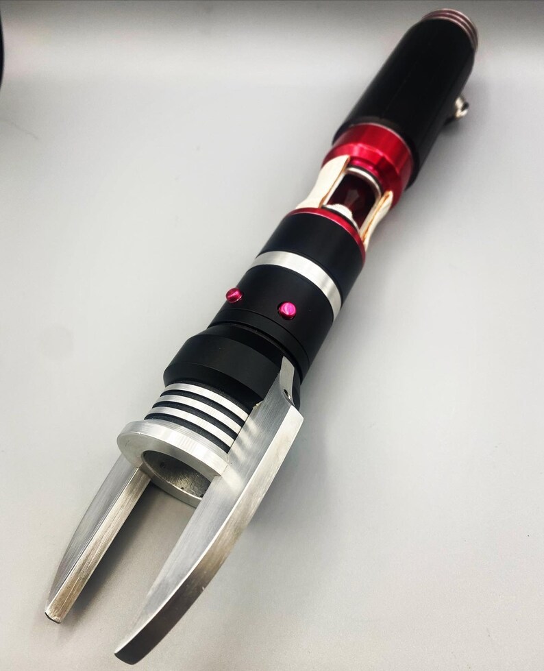 May include: A black and silver tool with a red accent and a claw-like end. The tool has a silver ring around the middle and a red button on the side.
