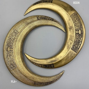 May include: Two golden crescent-shaped objects with intricate engraved patterns. The top object is labeled "RESIN" and the bottom object is labeled "PLA+". The objects are displayed on a gray background.