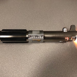 May include: A silver lightsaber with a black handle and a red blade. The lightsaber is turned on and the blade is glowing.