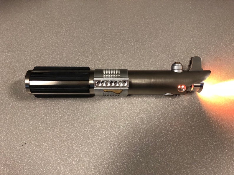 May include: A silver lightsaber with a black handle and a red blade. The lightsaber is turned on and the blade is glowing.