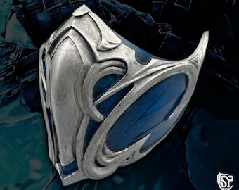 May include: A silver and blue mask with intricate details. The mask has a blue gem in the center and a silver frame.
