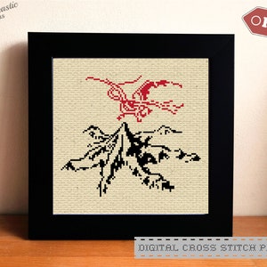 May include: A digital cross stitch pattern featuring a black and white mountain scene with a red bird flying above. The pattern is framed and displayed on a wooden surface.  DIGITAL CROSS STITCH PATTERN