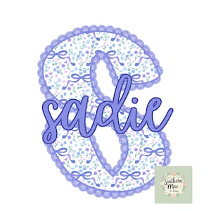 May include: A floral design with the name "Sadie" in a cursive font. The name is in a light purple color, and the floral design has a white background with blue and purple flowers and ribbons. The design is surrounded by a purple lace border.