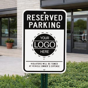 May include: A rectangular black and white metal sign with rounded corners, reading "RESERVED PARKING". It features a circular space for a logo and the text "VIOLATORS WILL BE TOWED AT VEHICLE OWNER'S EXPENSE". The sign is mounted on a green metal post.