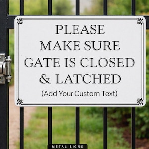 May include: A rectangular white metal sign with black text that reads "PLEASE MAKE SURE GATE IS CLOSED & LATCHED (Add Your Custom Text)". The sign is framed with a decorative border and mounted on a black metal gate.