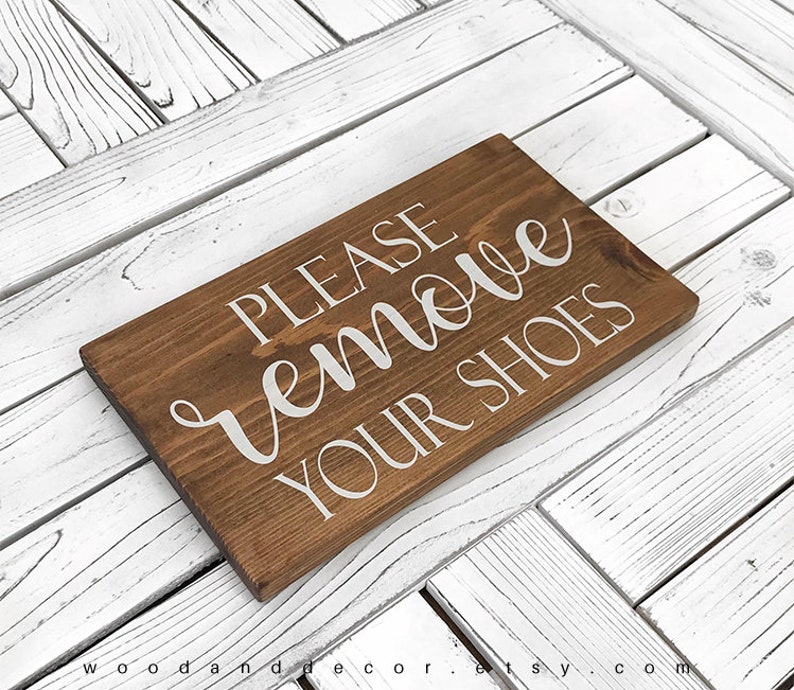 May include: A brown wooden sign with white text that reads "PLEASE remove YOUR SHOES".