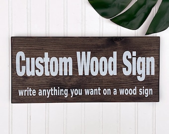 May include: A dark brown wooden sign with white text that reads "Custom Wood Sign write anything you want on a wood sign".