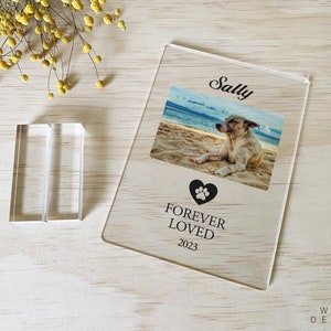 Peut inclure: Un cadre photo en acrylique transparent avec un c&oelig;ur noir en forme de patte et le texte "Forever Loved 2023". Le cadre contient une photo d'un chien nomm&eacute; Sally sur une plage.
