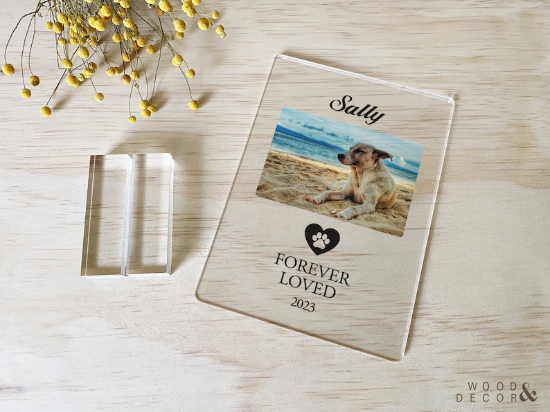 Peut inclure: Un cadre photo en acrylique transparent avec un c&oelig;ur noir en forme de patte et le texte "Forever Loved 2023". Le cadre contient une photo d'un chien nomm&eacute; Sally sur une plage.