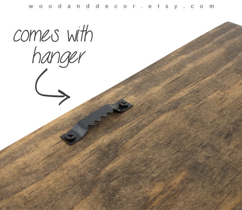 May include: The back of a wooden sign with a black metal hanger attached. The sign is made of dark brown wood with a natural grain pattern.