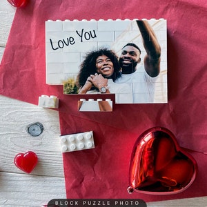 Puede incluir: Un rompecabezas de bloques blancos con una foto de una pareja tomando una selfie. El rompecabezas est&aacute; parcialmente ensamblado y las palabras "Love You" est&aacute;n escritas en la parte superior del rompecabezas.