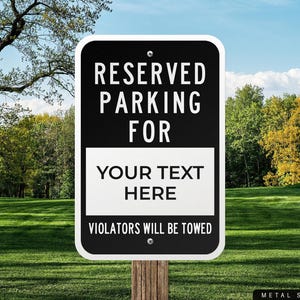 May include: A black and white metal sign with rounded corners, reading "RESERVED PARKING FOR YOUR TEXT HERE" in white capital letters. The bottom of the sign states "VIOLATORS WILL BE TOWED". The sign is mounted on a wooden post.