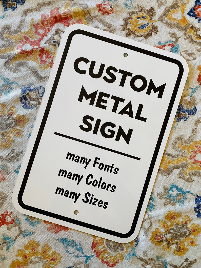 Pu&ograve; includere: Cartello in metallo bianco con testo nero che recita "CUSTOM METAL SIGN" e "many Fonts, many Colors, many Sizes".