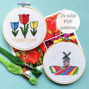 May include: Two embroidery hoop kits with cross stitch patterns. One kit features a red, blue, and yellow tulip design with the word "Nederland" in orange. The other kit features a windmill and rainbow stripes. The text "2x tulip PDF patterns" is written on a card behind the hoops.