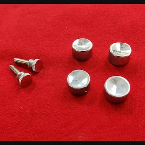 May include: A set of six silver-colored metal hardware components consisting of two threaded screws with knurled heads and four matching cylindrical caps with smooth, slightly concave tops and textured, knurled sides for grip.