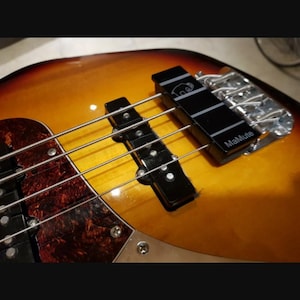 May include: A sunburst finish electric bass guitar body featuring a tortoiseshell pickguard, a black single-coil pickup, and a black bridge mute accessory labelled MaMute with a small white elephant icon printed on the top surface.