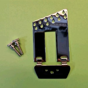 May include: A chrome-plated guitar bridge assembly featuring a rectangular frame with a slanted top edge containing six string holes, a central cutout, and a hinged tailpiece section with three mounting holes, accompanied by two threaded metal screws.
