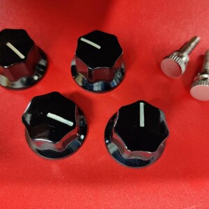 May include: Four black, circular control knobs with a glossy finish and a single white indicator line on the top surface. Each knob features a ridged, multi-faceted edge. Two silver-colored metal screws with flat, circular heads are included.