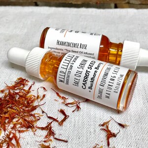 May include: Two amber glass bottles with droppers containing face oil serum. The bottles are labeled "WILD ELIXIRS" and "FRANKINCENSE ROSE". The text on the label reads "FACE OIL SERUM CARROT SEED + Buckthorn Berry ORGANIC REJUVENATING MATURING SKIN 0.5 FL OZ/15ML".