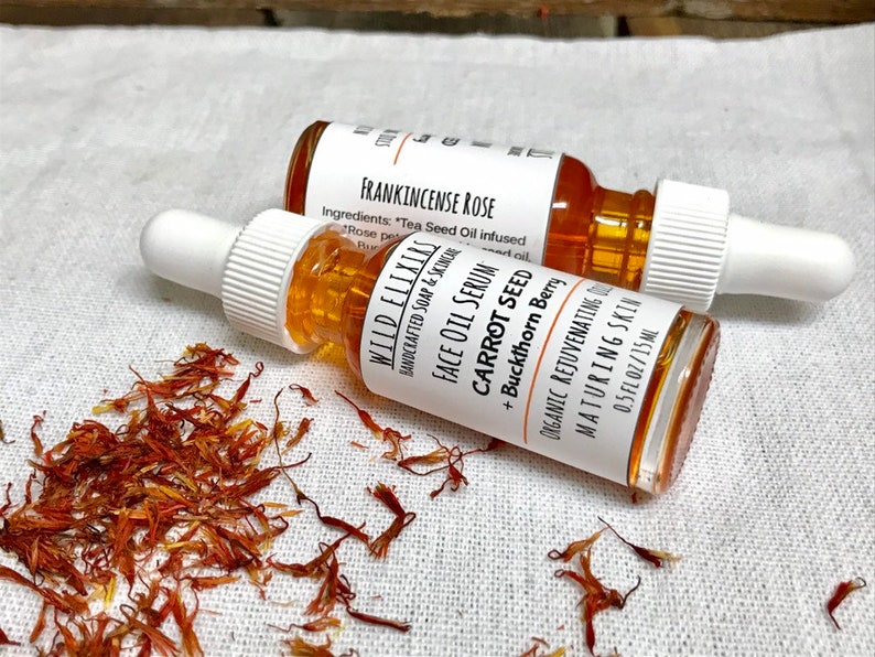 May include: Two amber glass bottles with droppers containing face oil serum. The bottles are labeled "WILD ELIXIRS" and "FRANKINCENSE ROSE". The text on the label reads "FACE OIL SERUM CARROT SEED + Buckthorn Berry ORGANIC REJUVENATING MATURING SKIN 0.5 FL OZ/15ML".