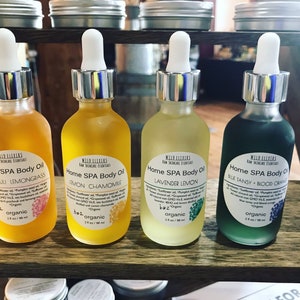 May include: Four glass bottles of organic essential oil blends for home spa use. The bottles are labeled with the names of the blends: Patchouli Lemongrass, Lemon Chamomile, Lavender Lemon, and Blue Tansy + Blood Orange. Each bottle is 2 oz.