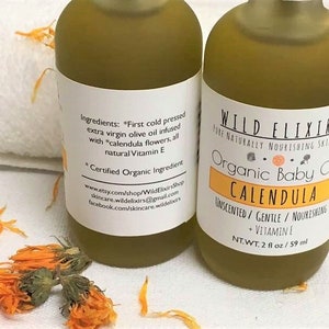 Puede incluir: Dos botellas de vidrio &aacute;mbar de aceite de beb&eacute; org&aacute;nico de cal&eacute;ndula con etiquetas blancas. La etiqueta de la botella delantera dice "Wild Elixirs Pure Naturally Nourishing Skincare Organic Baby Oil Calendula Unscented/Gentle/Nourishing + Vitamin E NT.WT. 2 fl oz/59 ml". La etiqueta de la botella trasera enumera los ingredientes, "First cold pressed extra virgin olive oil infused with *calendula flowers, all natural Vitamin E *Certified Organic Ingredient" y la informaci&oacute;n de contacto de la empresa.