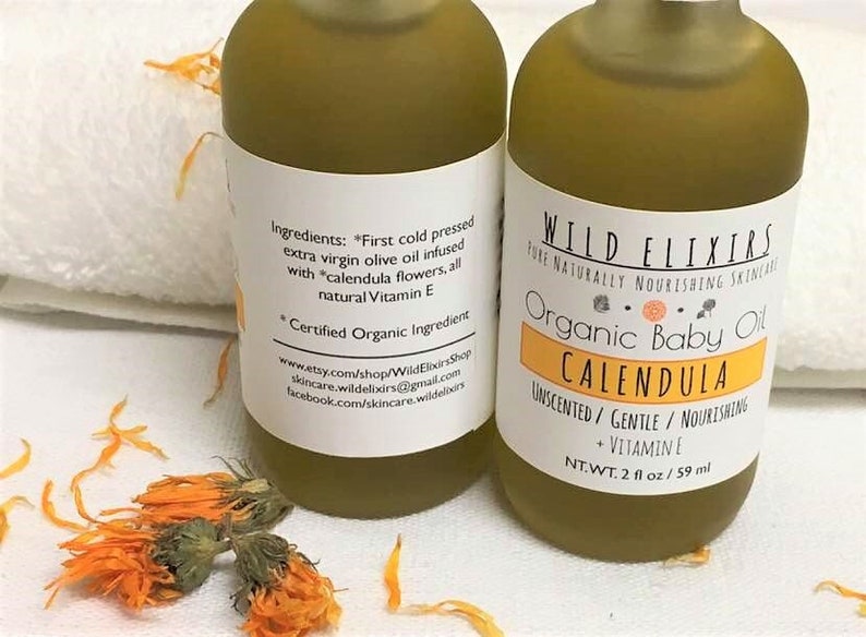 Puede incluir: Dos botellas de vidrio &aacute;mbar de aceite de beb&eacute; org&aacute;nico de cal&eacute;ndula con etiquetas blancas. La etiqueta de la botella delantera dice "Wild Elixirs Pure Naturally Nourishing Skincare Organic Baby Oil Calendula Unscented/Gentle/Nourishing + Vitamin E NT.WT. 2 fl oz/59 ml". La etiqueta de la botella trasera enumera los ingredientes, "First cold pressed extra virgin olive oil infused with *calendula flowers, all natural Vitamin E *Certified Organic Ingredient" y la informaci&oacute;n de contacto de la empresa.