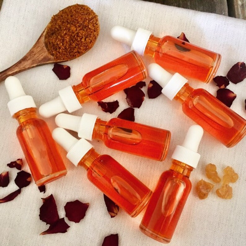May include: Seven small amber glass bottles with droppers filled with a bright orange liquid. The bottles are arranged on a white surface with rose petals and a small pile of brown sugar.