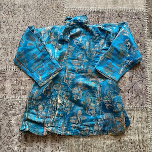 Puede incluir: Una chaqueta de brocado azul y dorado con cuello mandar&iacute;n y mangas largas. La chaqueta est&aacute; decorada con un patr&oacute;n floral.