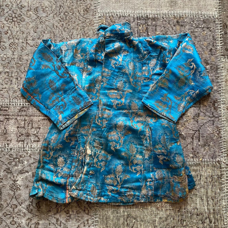 Puede incluir: Una chaqueta de brocado azul y dorado con cuello mandar&iacute;n y mangas largas. La chaqueta est&aacute; decorada con un patr&oacute;n floral.